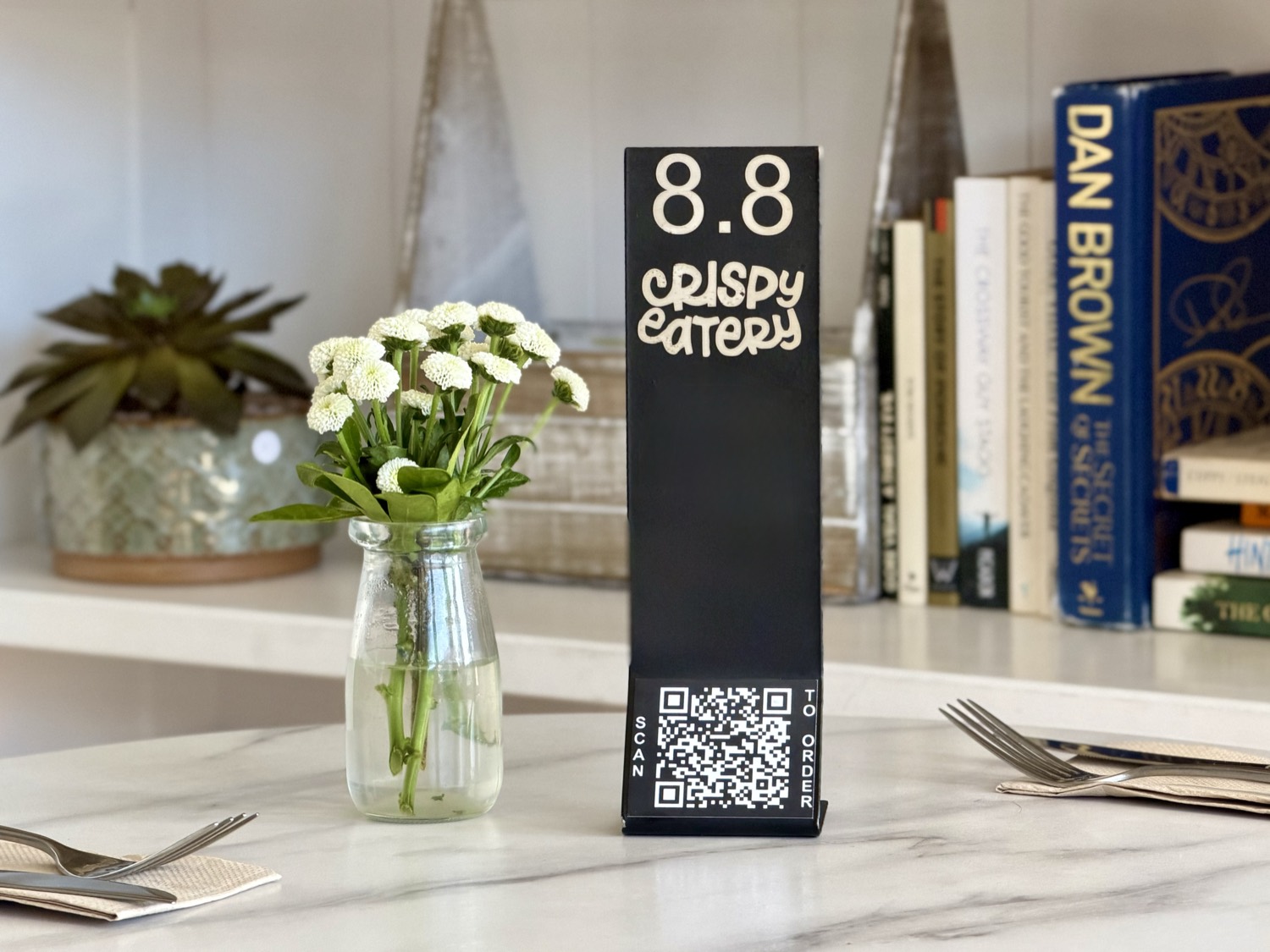 A Crispy Eatery QR table stand for table 8.8 reading ‘Scan to order’ on a marble café table in Remuera, Auckland.
